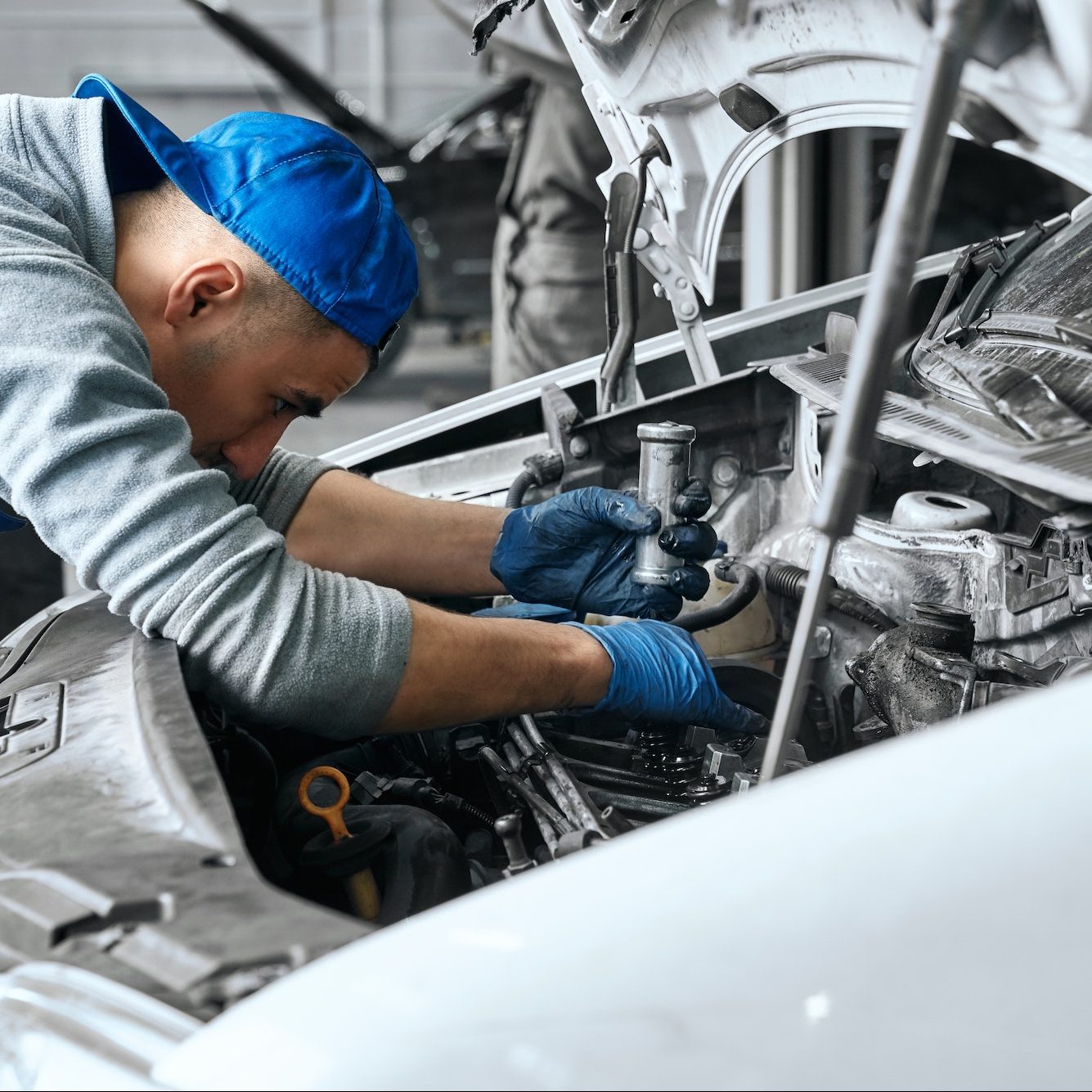 Mechanic in blue overalls checking serviceability of car engine - Tecnológico Universitario Rumiñahui Mechanic in blue overalls checking serviceability of car engine